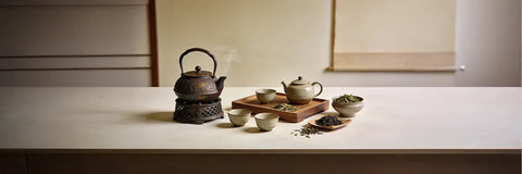 A complete Japanese tetsubin tea set laid out on a wooden surface, showing the cast iron teapot, matching cups, trivet, and infuser basket.