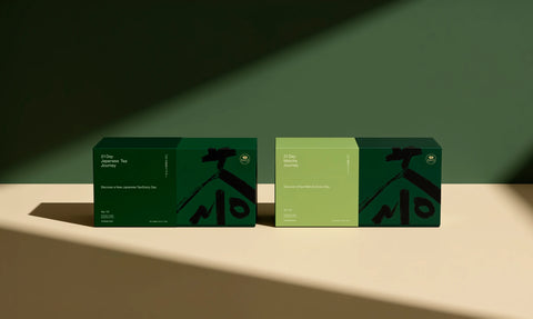 Two rectangular tea boxes displayed side by side on a beige surface against a dark green wall, with dramatic diagonal lighting casting shadows. The left box is dark green and the right box is light green; both feature black abstract graphic elements and white text.